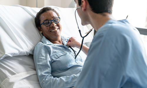 doctor listens to a woman's chest on hospital bed