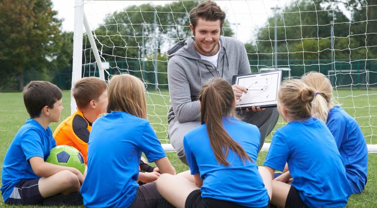 Coach with clipboard in front of goal with kids