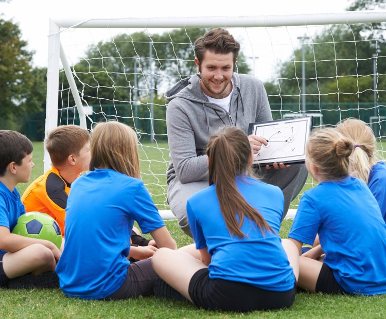 Coach with clipboard in front of goal with kids