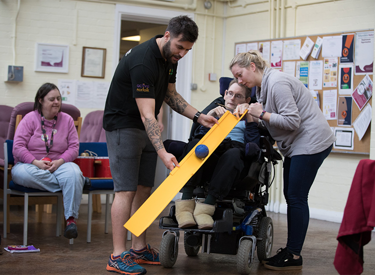 man and centre staff worker hold ramp for disabled man to play bowls