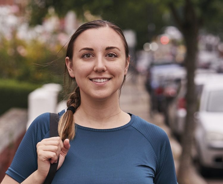 woman with yoga mat walking down city street