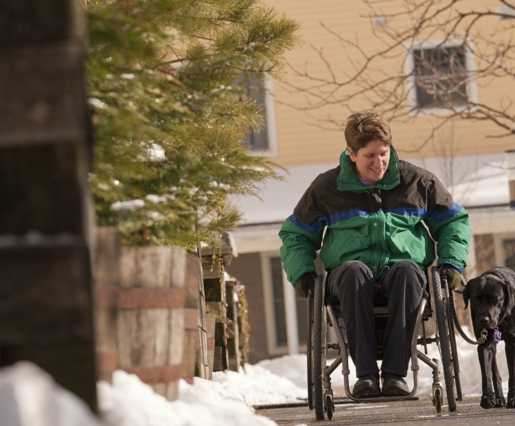 woman in wheelchair walking dog down snowy street