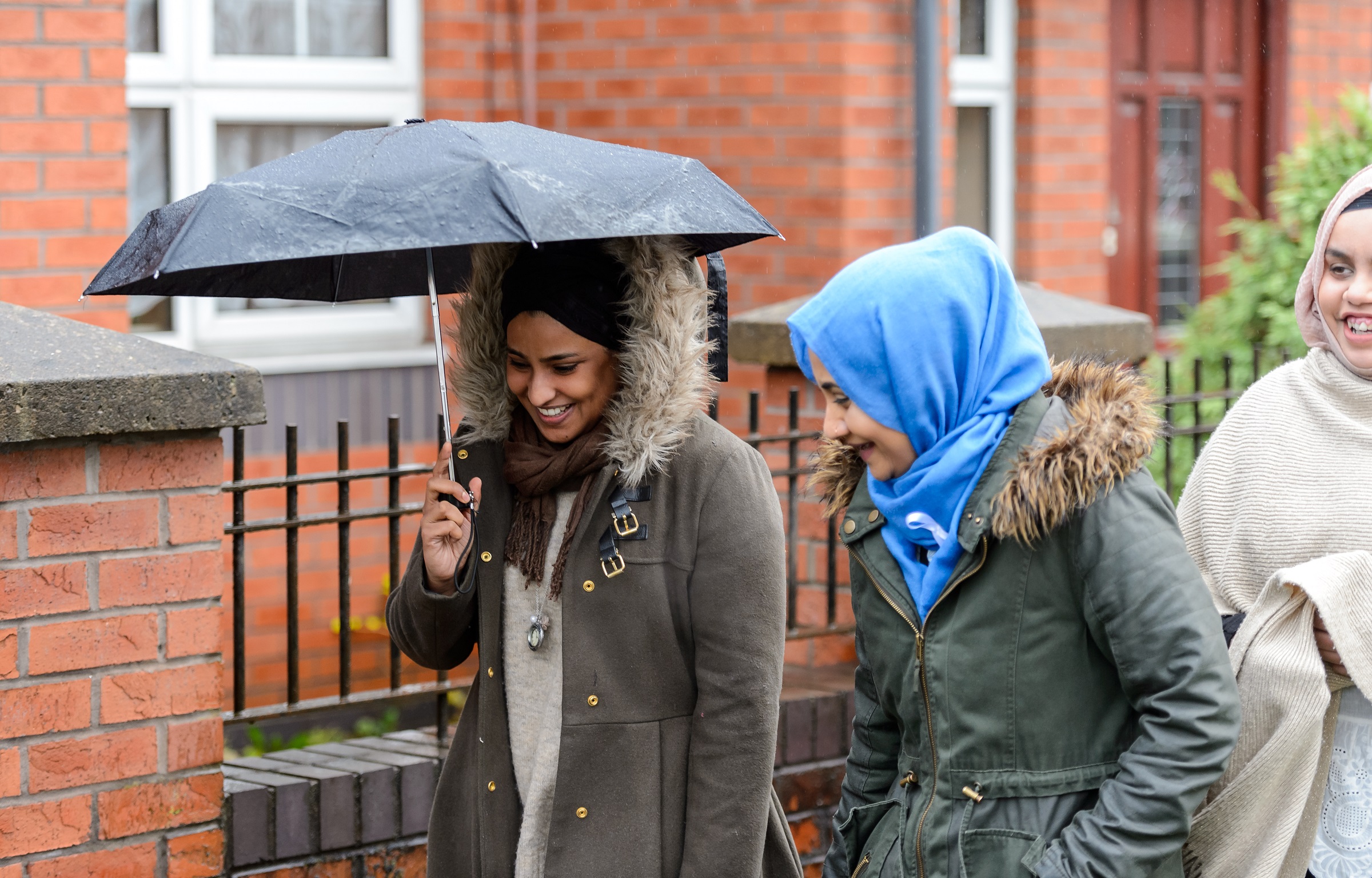 three women walking down street with umbrella