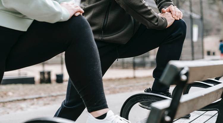 two people stretching legs on a park bench